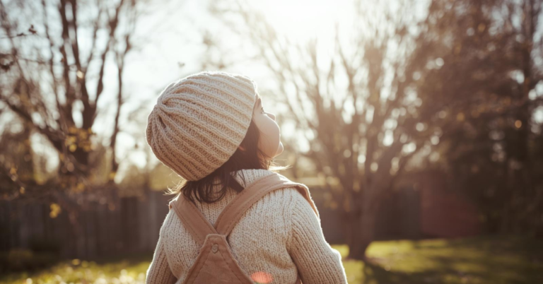 Toddler girl in a winter hat and overall standing in a garden looking up at the sky for the first time during her adoption journey