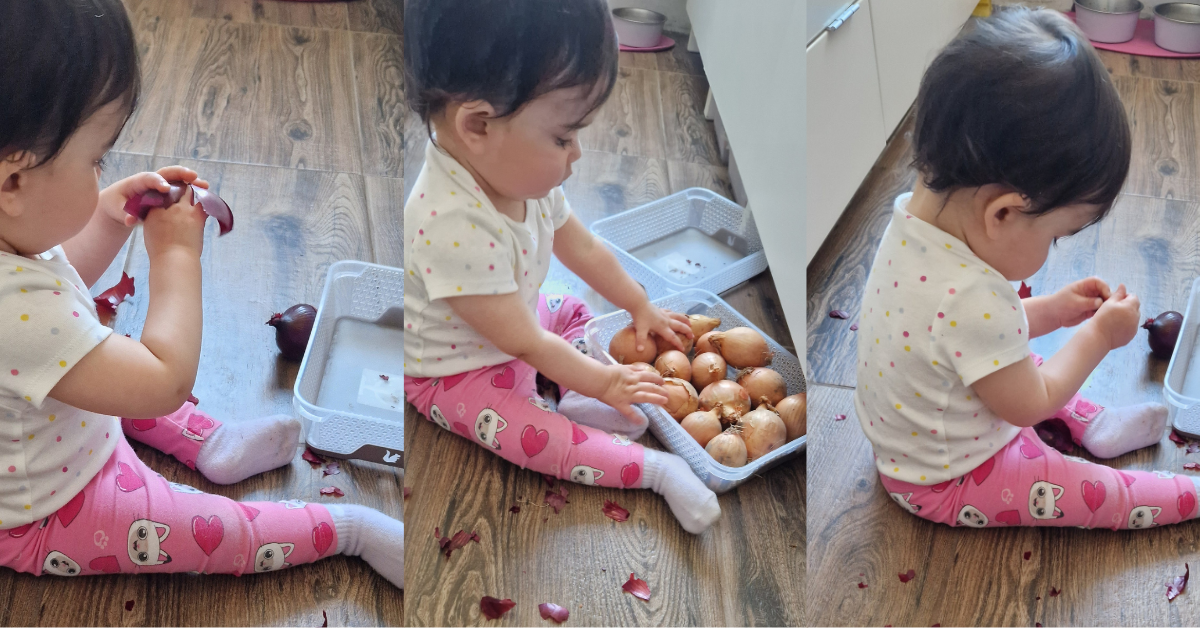 A toddler sitting on a kitchen floor sorting onions in and out of a box, completely absorbed — a simple and free toddler learning activity using everyday household items.