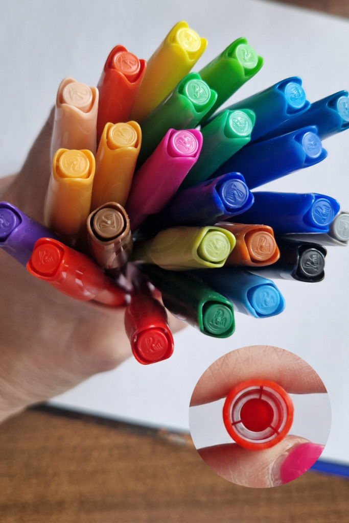A hand holding a bundle of colorful washable markers with ventilated caps, a safety feature designed to allow airflow if a child accidentally swallows the cap