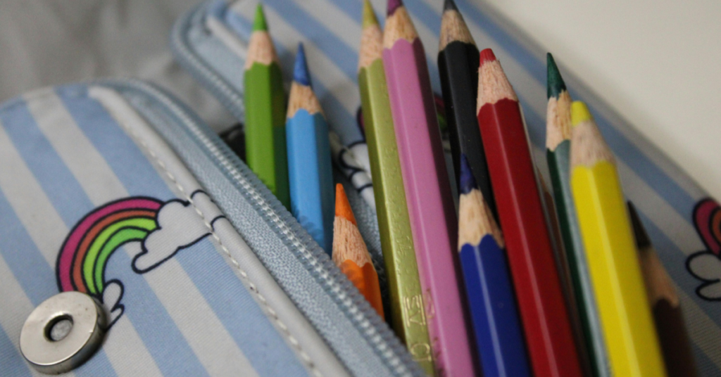 Close-up of a zippered pencil case with a rainbow print, filled with colorful sharpened pencils.