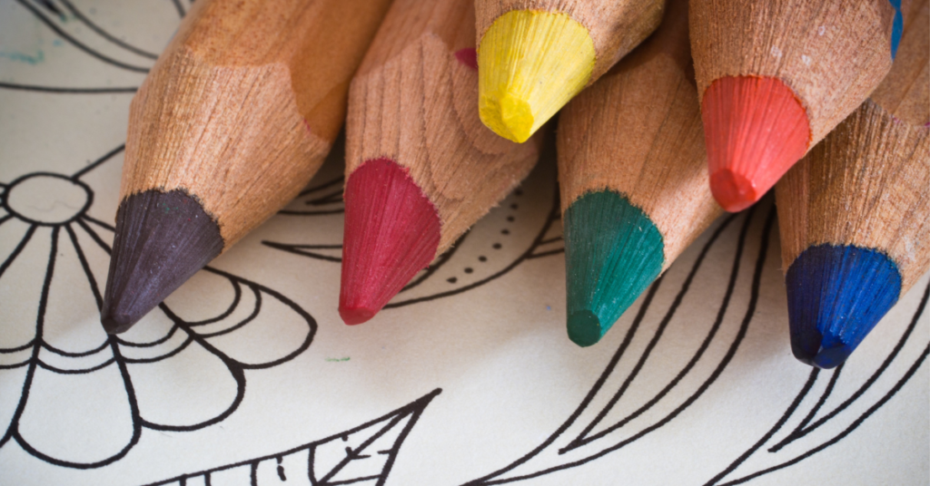 Sharpened standard colored pencils in six colors resting on a coloring page, the size children move on to once their grip is stable